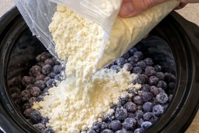 Thumbnail for Dumping dry lemon cake mix over frozen wild blueberries, together with 2 other ingredients, into slow cooker for a treat that’s my default when I do
